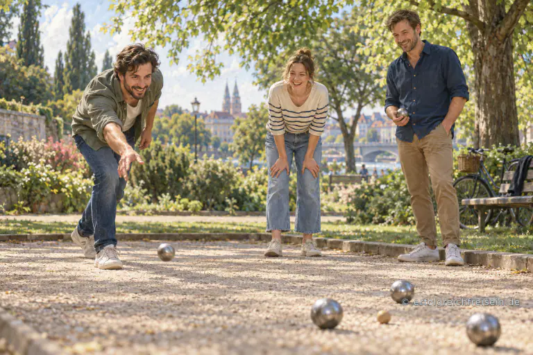 Drei Freunde spielen an einem sonnigen Nachmittag gemeinsam Boule in einem grünen Stadtpark.